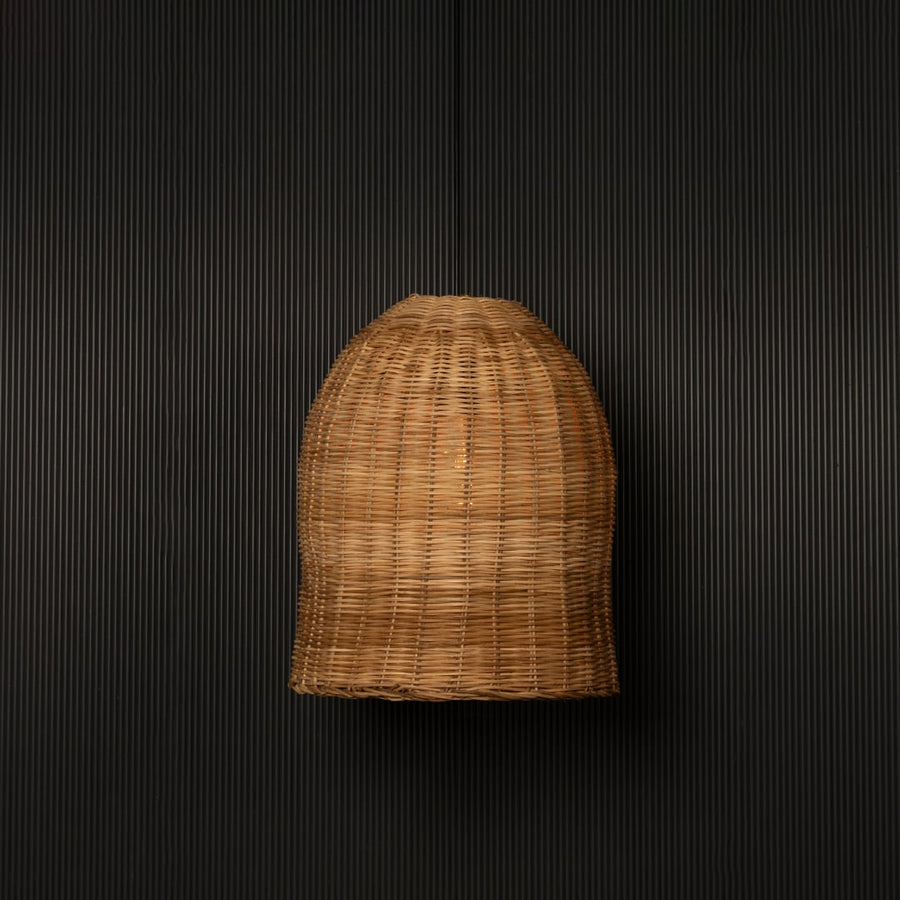 Dome-shaped rattan pendant light with handwoven bamboo shade turned on glowing softly against black background.