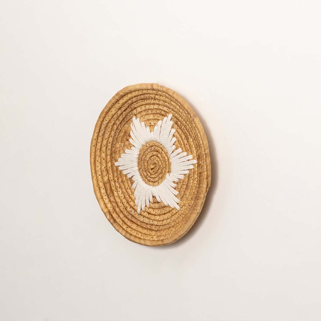 Side profile of the flat woven wall basket showing the thick natural fiber coils and white wrapping details on a white surface.