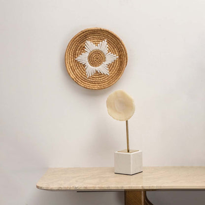 Medium beige and white woven wall basket hanging on a white wall above a marble console table with a sculpture for boho home decor styling.