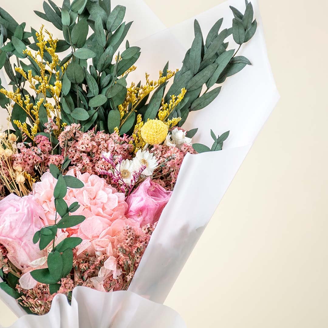 Closeup of dried bouquet featuring infinity rose hydrangea crystal grass billy ball and eucalyptus in pink yellow green mix.