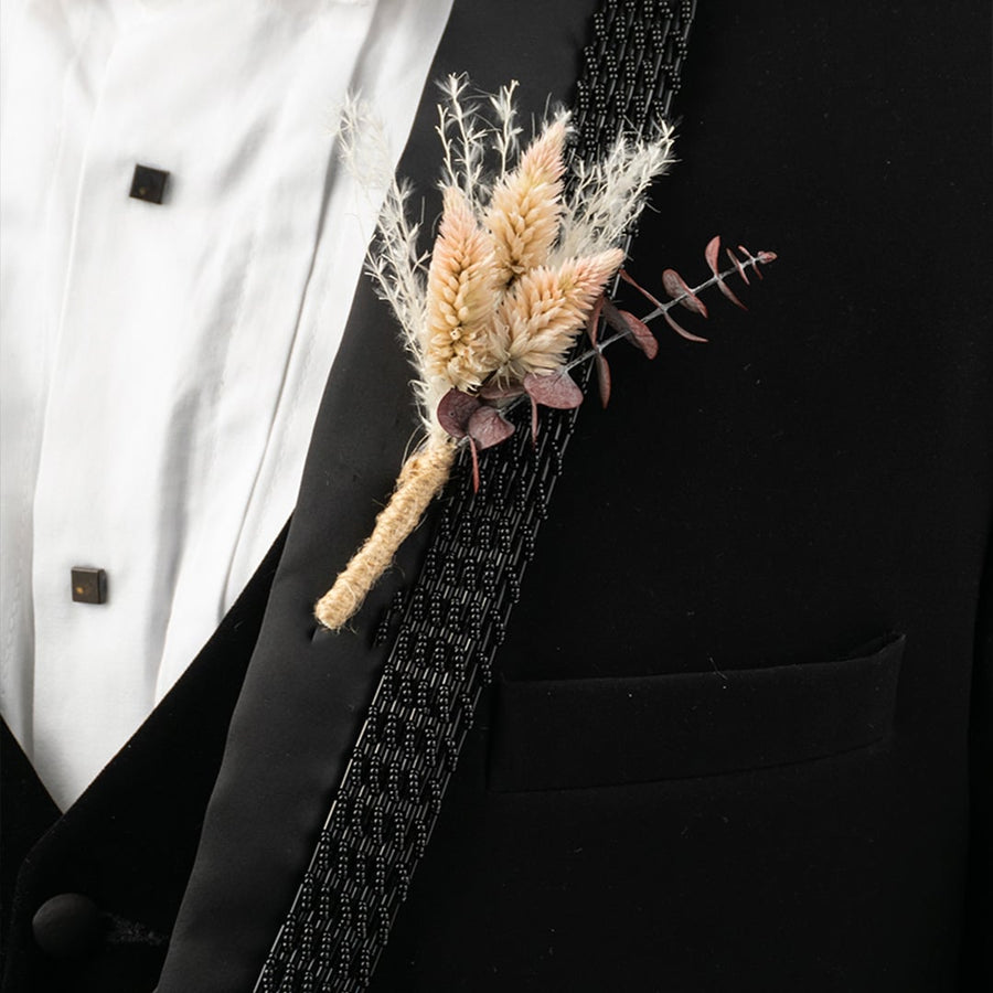 Closeup of elegant wheat boutonniere for men in black suit jacket wedding groom accessory.