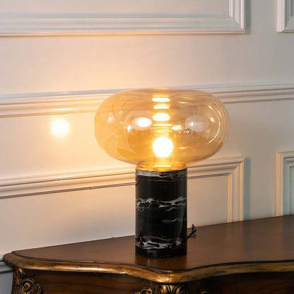 Amber smoked glass table lamp with black marble base and exposed bulb creating elegant contemporary decorative lighting.