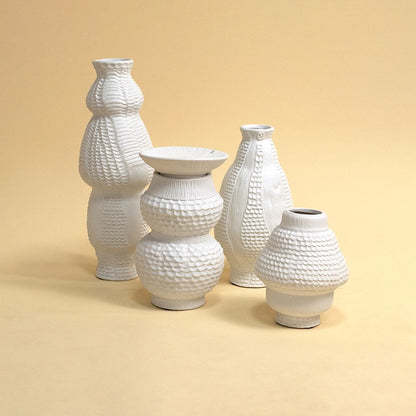 Set of sculptural white textured vases arranged under soft lighting highlighting artistic craftsmanship and organic design appeal.