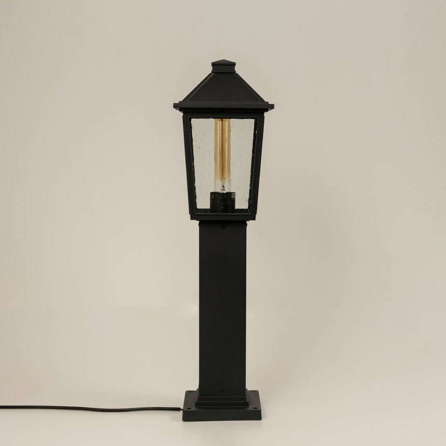 A tall black outdoor post light turned off on a white background highlighting its rectangular glass panels and sturdy metal frame with a clean minimal backdrop.