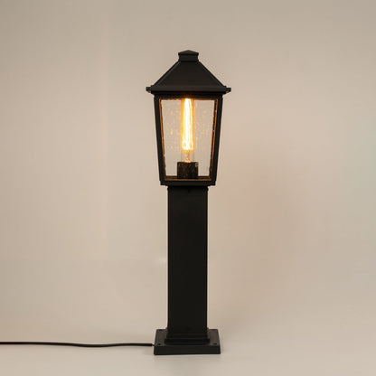 Modern black outdoor bollard light with warm glowing bulb for elegant pathway decor styling use.