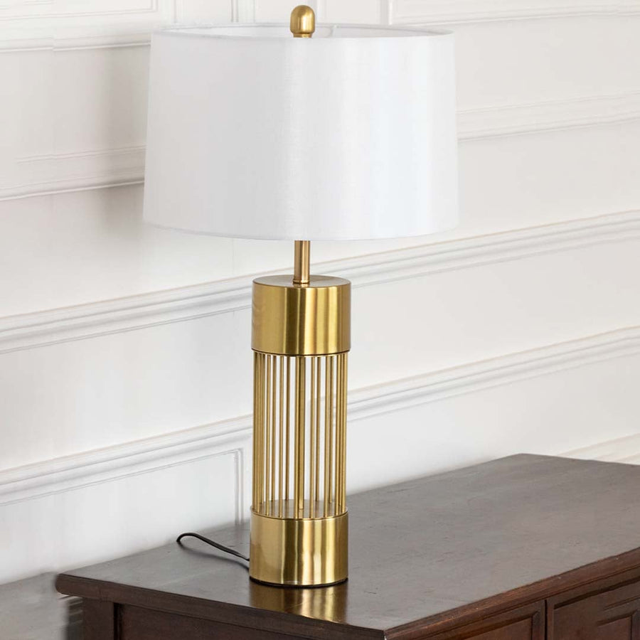 Tall gold lamp with clear glass accents on wooden table with light off and white wall background for luxury minimalist décor.