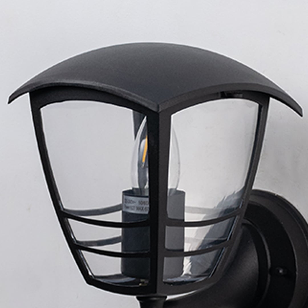 Black metal outdoor wall light closeup image with clear curved glass panels and protective wire cage for porch decor.