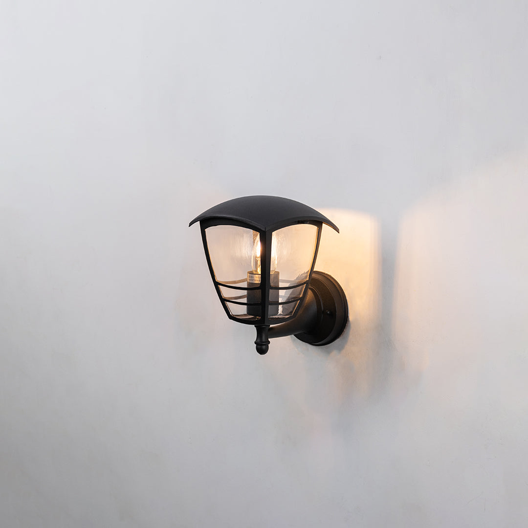Black metal outdoor wall light on white background featuring a compact curved glass shade hood design for porch decor.