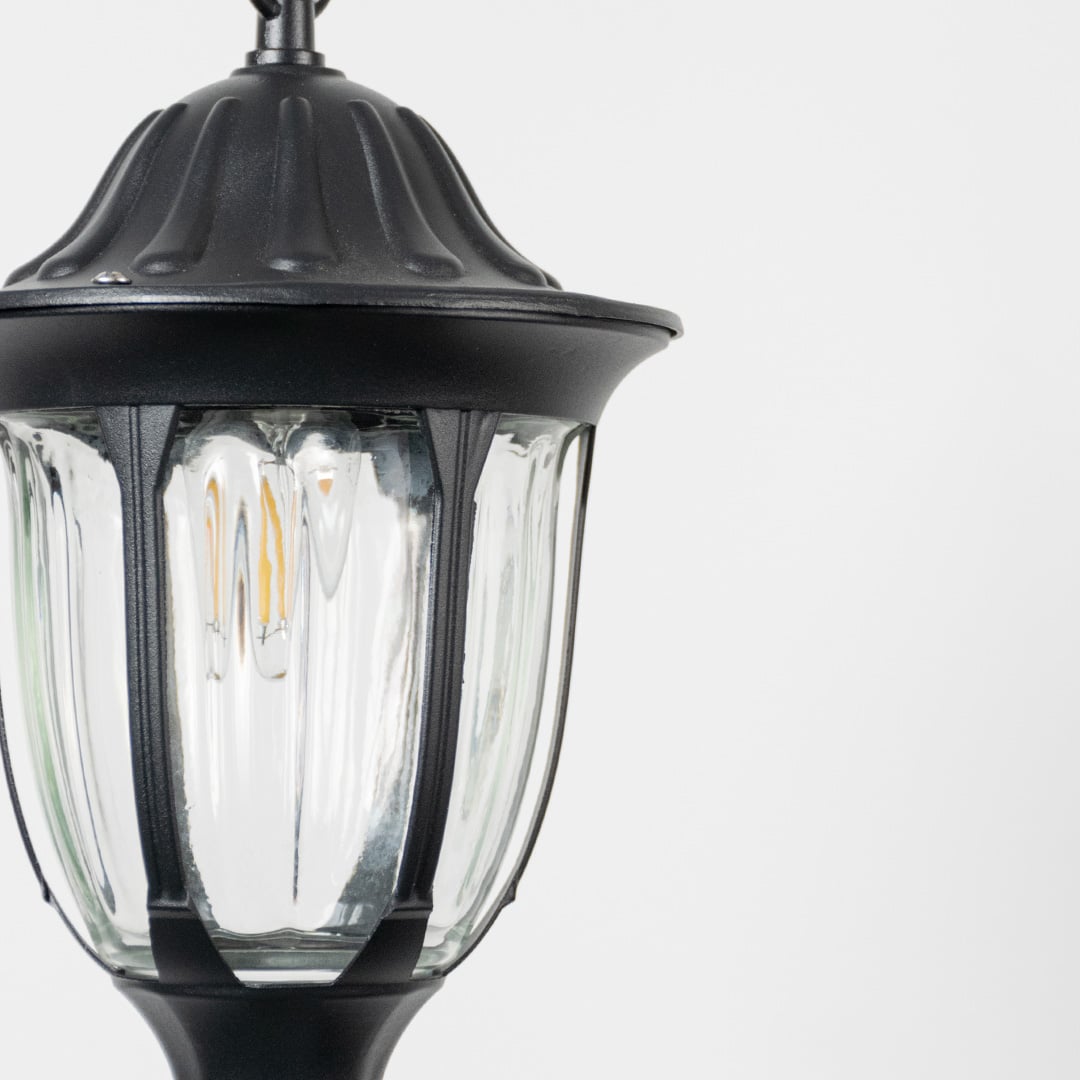 Closeup view of black hanging lantern light highlighting bulb detail and curved glass panels.