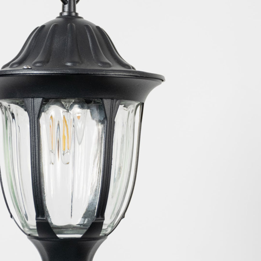 Closeup view of black hanging lantern light highlighting bulb detail and curved glass panels.