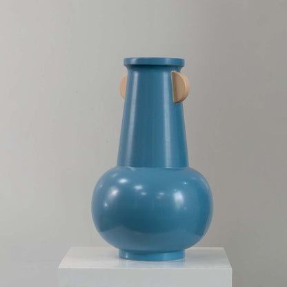 Blue modern metal vase with rounded base and sculpted handles displayed on a clean white background highlighting its shape.