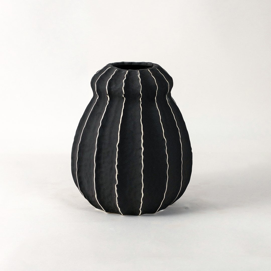 Minimal Noir ceramic vase on white background accentuating its curvy silhouette and artistic white-lined texture.