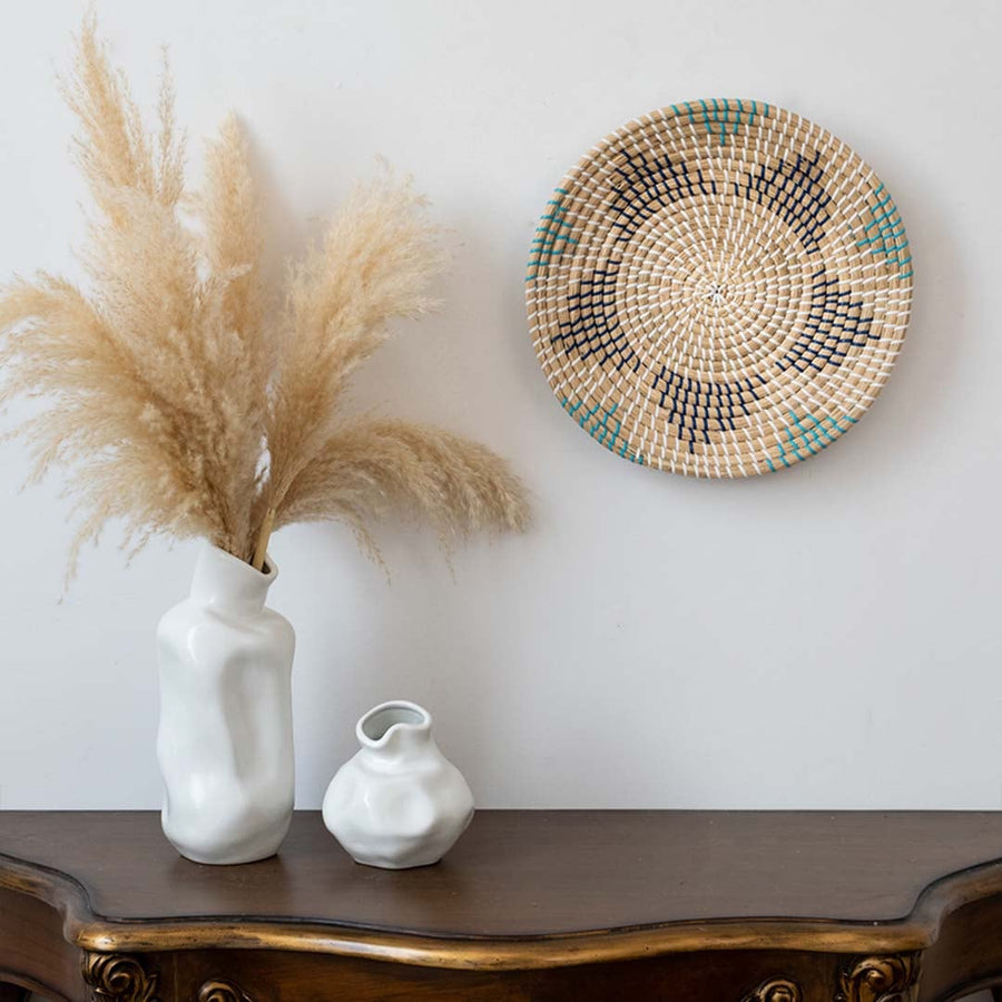 Handwoven wall basket decor in natural beige with blue and black pattern styled above console table for boho wall.