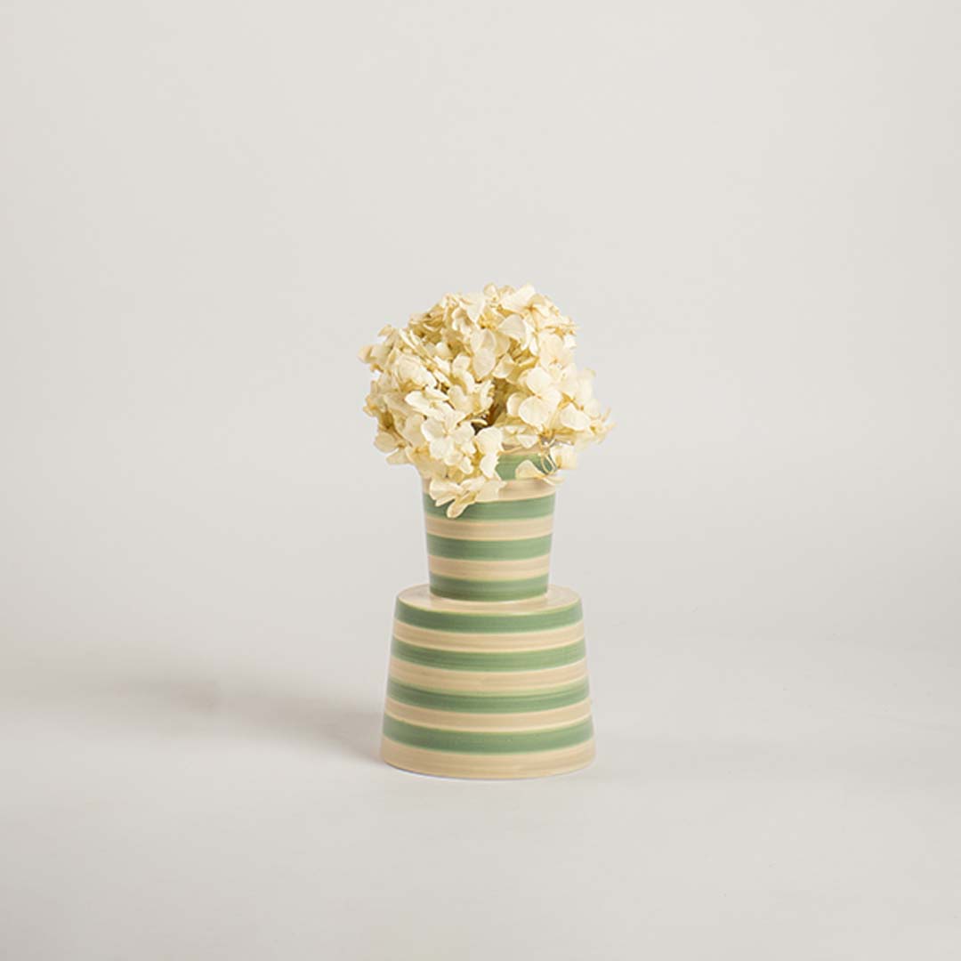 Contemporary striped ceramic vase in green and beige set on a plain white backdrop  emphasizing its modern shape and decorative appeal.