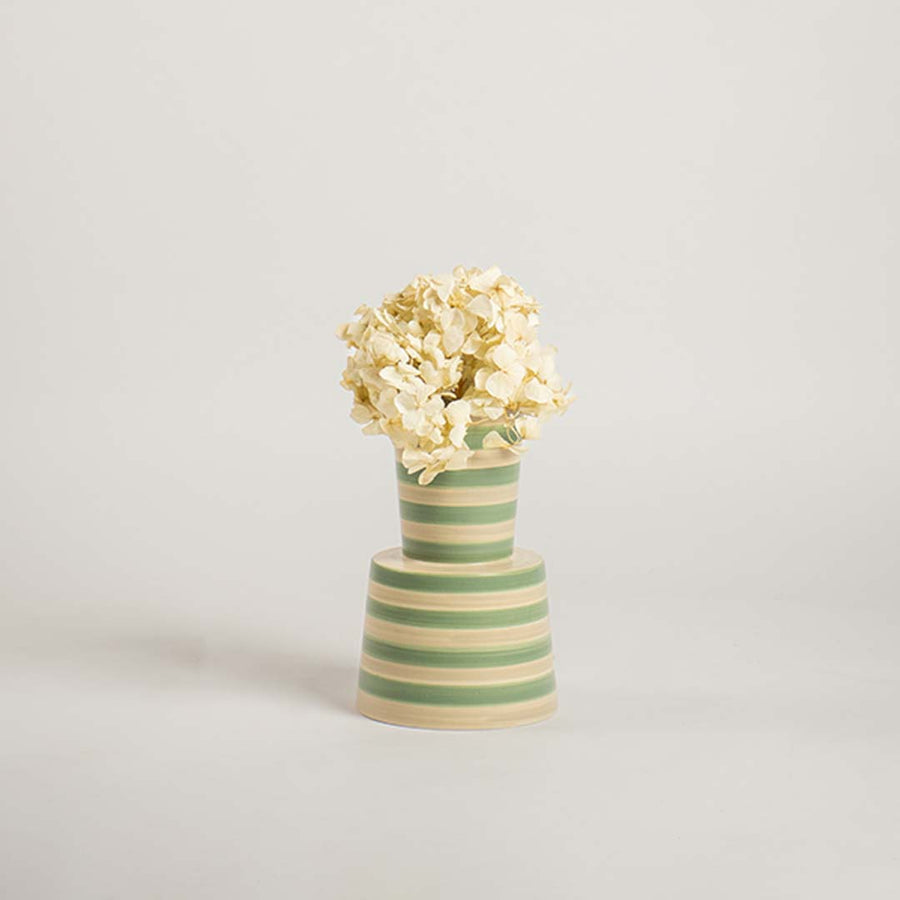 Contemporary striped ceramic vase in green and beige set on a plain white backdrop  emphasizing its modern shape and decorative appeal.