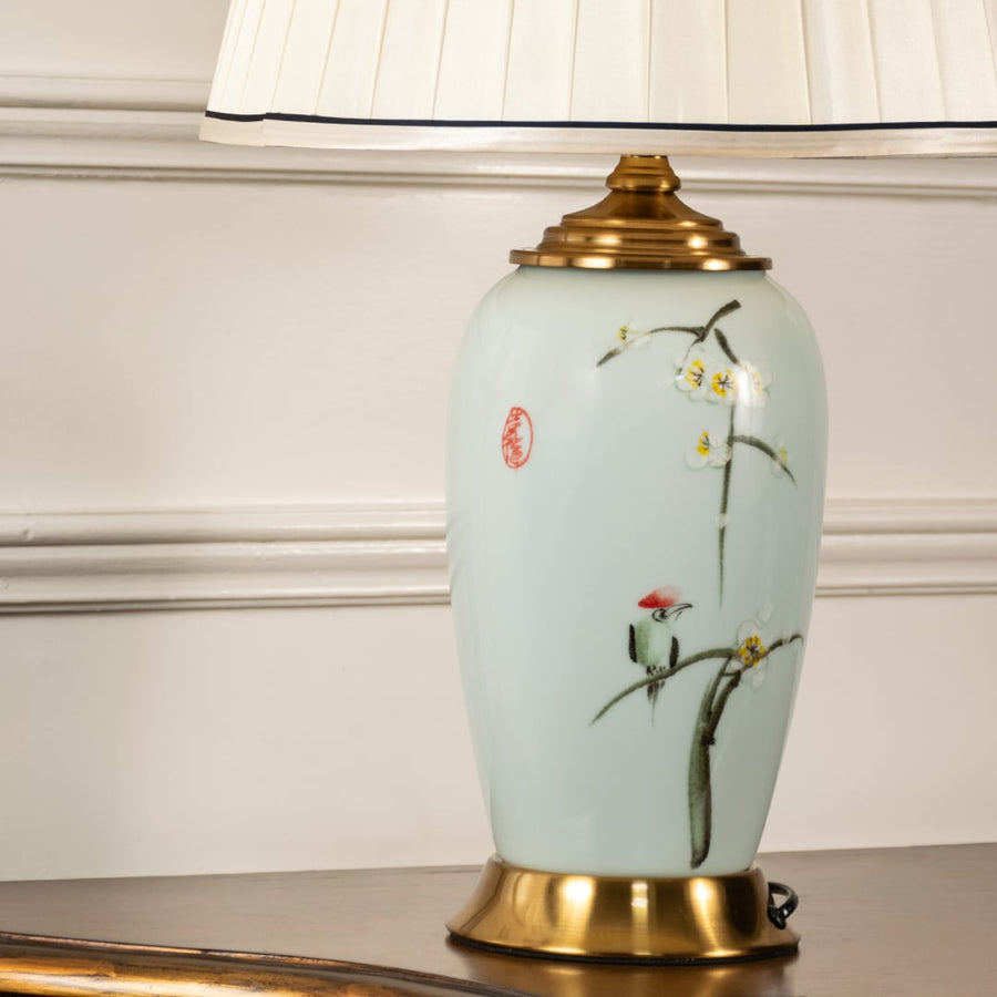 Closeup view highlighting intricate floral motifs on blue ceramic lamp body with a soft pleated shade and lustrous gold detailing for added luxury.
