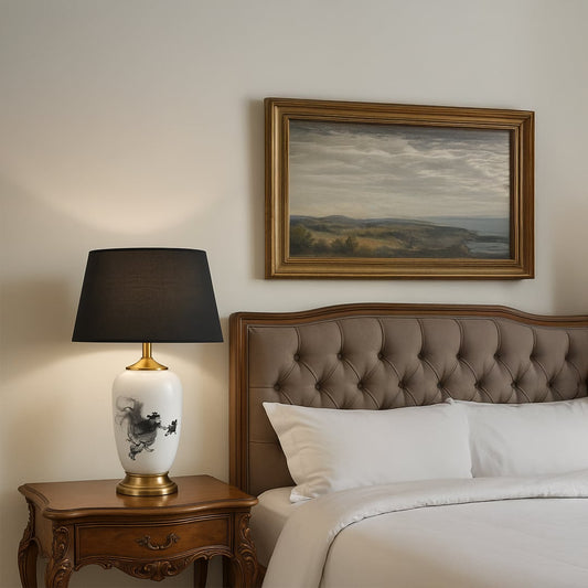 White ceramic table lamp with black abstract artwork gold base and black shade placed on a carved wooden bedside table adding a refined elegant touch to bedroom decor.
