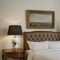 White ceramic table lamp with black abstract artwork gold base and black shade placed on a carved wooden bedside table adding a refined elegant touch to bedroom decor.