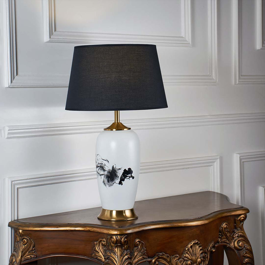 White ceramic table lamp with black abstract pattern gold base and black shade shown unlit on a white background highlighting its bold modern design.