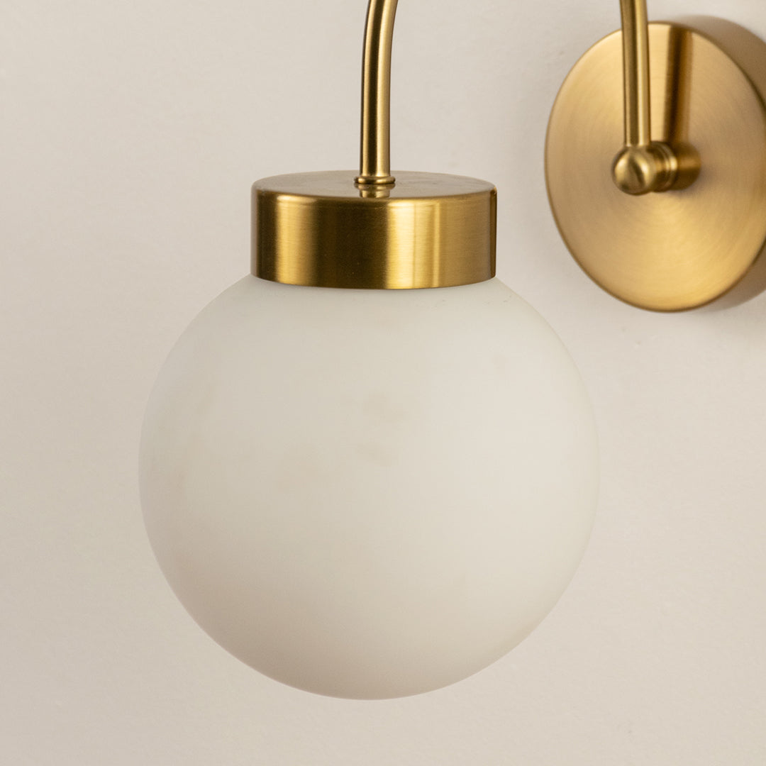 Wall light with gold mount and white glass globe on neutral background modern decorative lighting ideal for bedroom decor.
