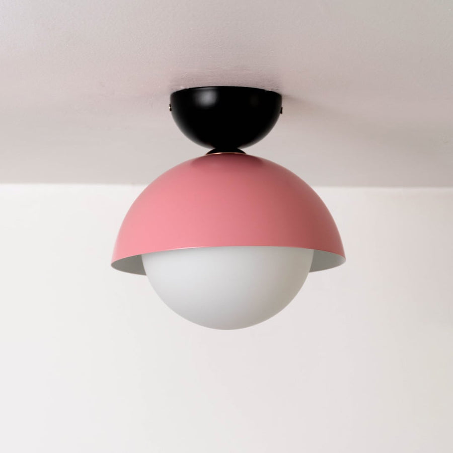 Ceiling light displayed off on a white background featuring a pink dome shade paired with a round white globe.