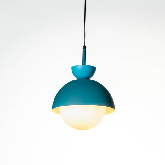 Minimal teal metal hanging pendant light with soft illuminated glass globe shade suspended on cord against plain white wall background for modern interiors.