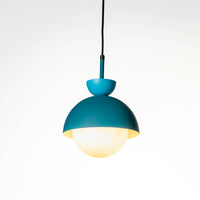Minimal teal metal hanging pendant light with soft illuminated glass globe shade suspended on cord against plain white wall background for modern interiors.