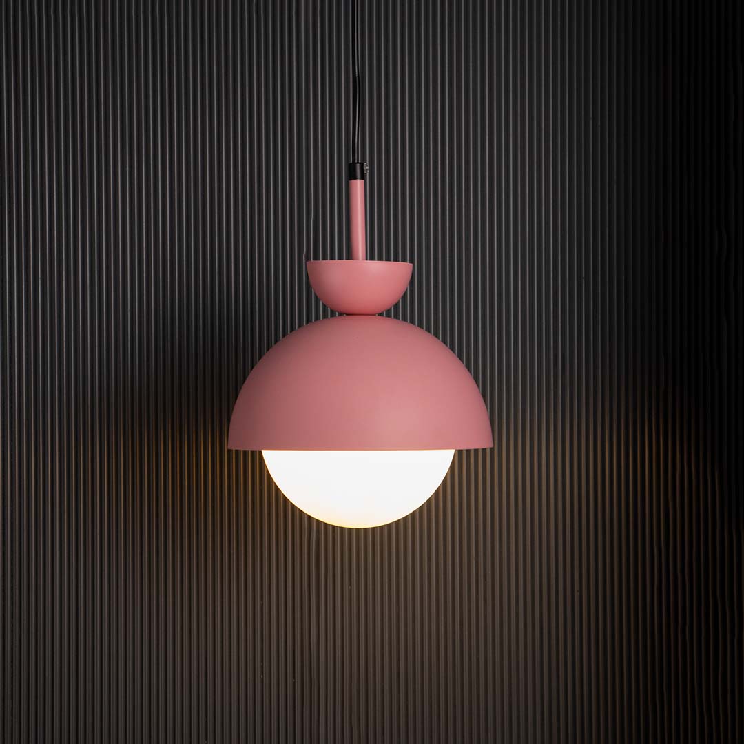 Contemporary pendant lamp in matte pink metal with frosted glass globe shade glowing beautifully against dark interiors