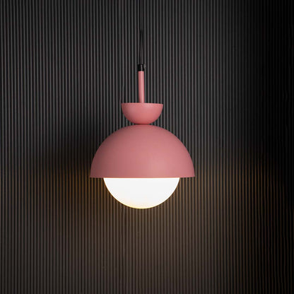 Contemporary pendant lamp in matte pink metal with frosted glass globe shade glowing beautifully against dark interiors