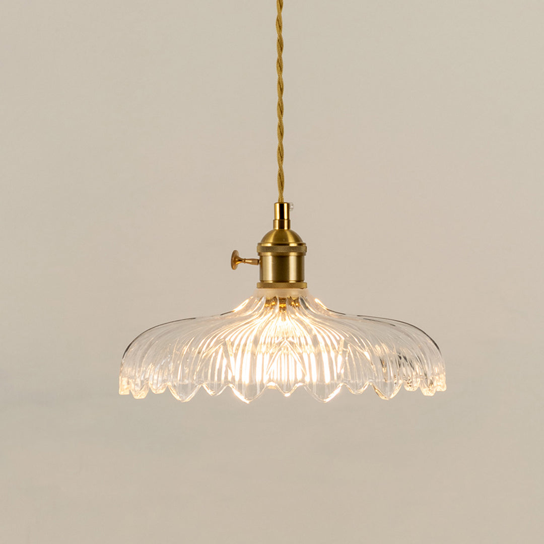 Illuminated clear patterned glass pendant light with gold fittings creating soft ambient lighting indoors.
