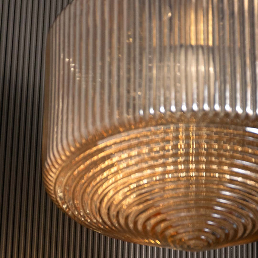 Closeup of ribbed amber glass pendant light capturing the textured vertical lines gold top and warm inner glow for modern decorative lighting.