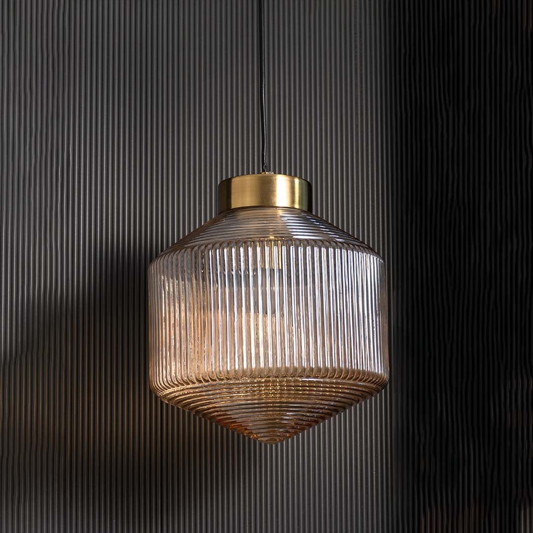 Amber ribbed glass pendant light shown with light off on a dark background highlighting its sculpted lines reflective surface and gold cap.