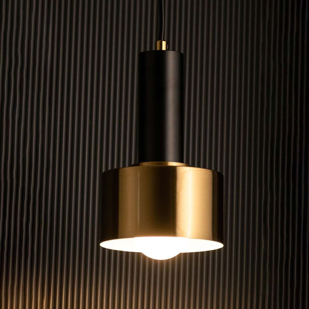 Metal pendant light in gold and black with bulb glowing softly against a dark background offering a warm modern accent for sophisticated spaces.