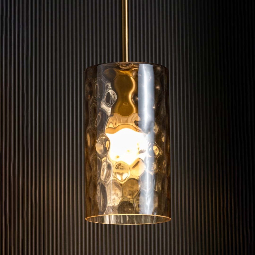 Amber glass pendant light glowing warmly against a dark black background highlighting its rich gold finish and textured glass design.