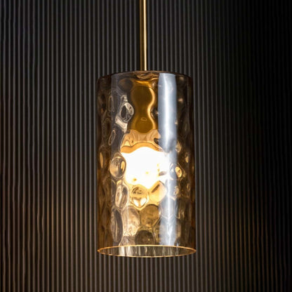 Amber glass pendant light glowing warmly against a dark black background highlighting its rich gold finish and textured glass design.