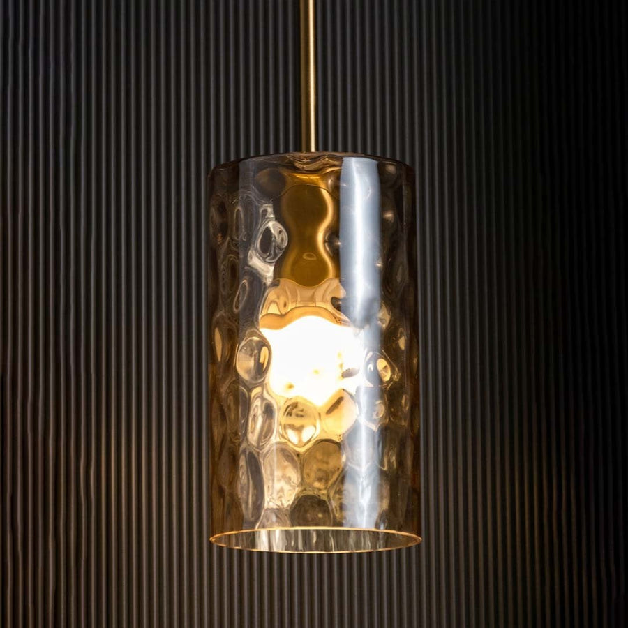 Amber glass pendant light glowing warmly against a dark black background highlighting its rich gold finish and textured glass design.
