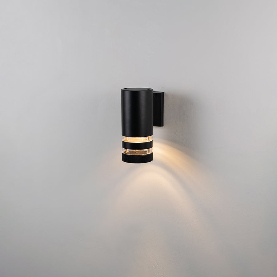 Black metal outdoor wall light on white background with warm upward downward glow for exterior decor.