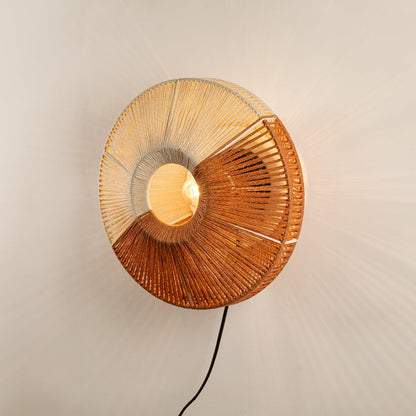 Round woven wall lamp with natural tones surrounding a central bulb glowing softly and adding a handcrafted warm accent that enriches the interior atmosphere.