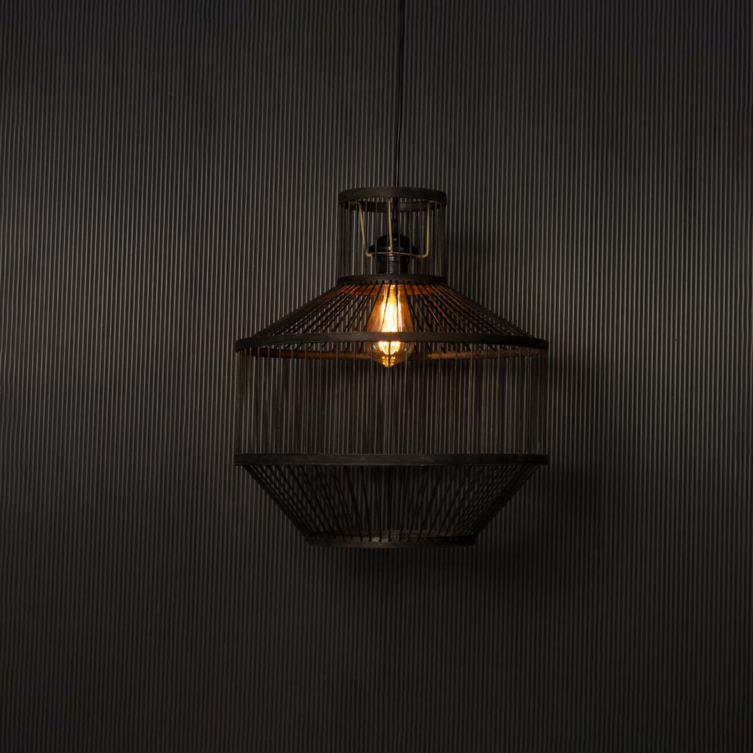 Black wire pendant light glowing warmly against black background highlighting industrial craftsmanship and soft radiance.