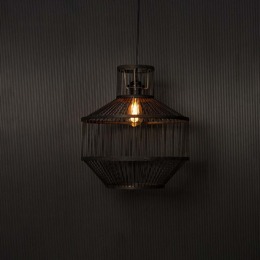Black wire pendant light glowing warmly against black background highlighting industrial craftsmanship and soft radiance.