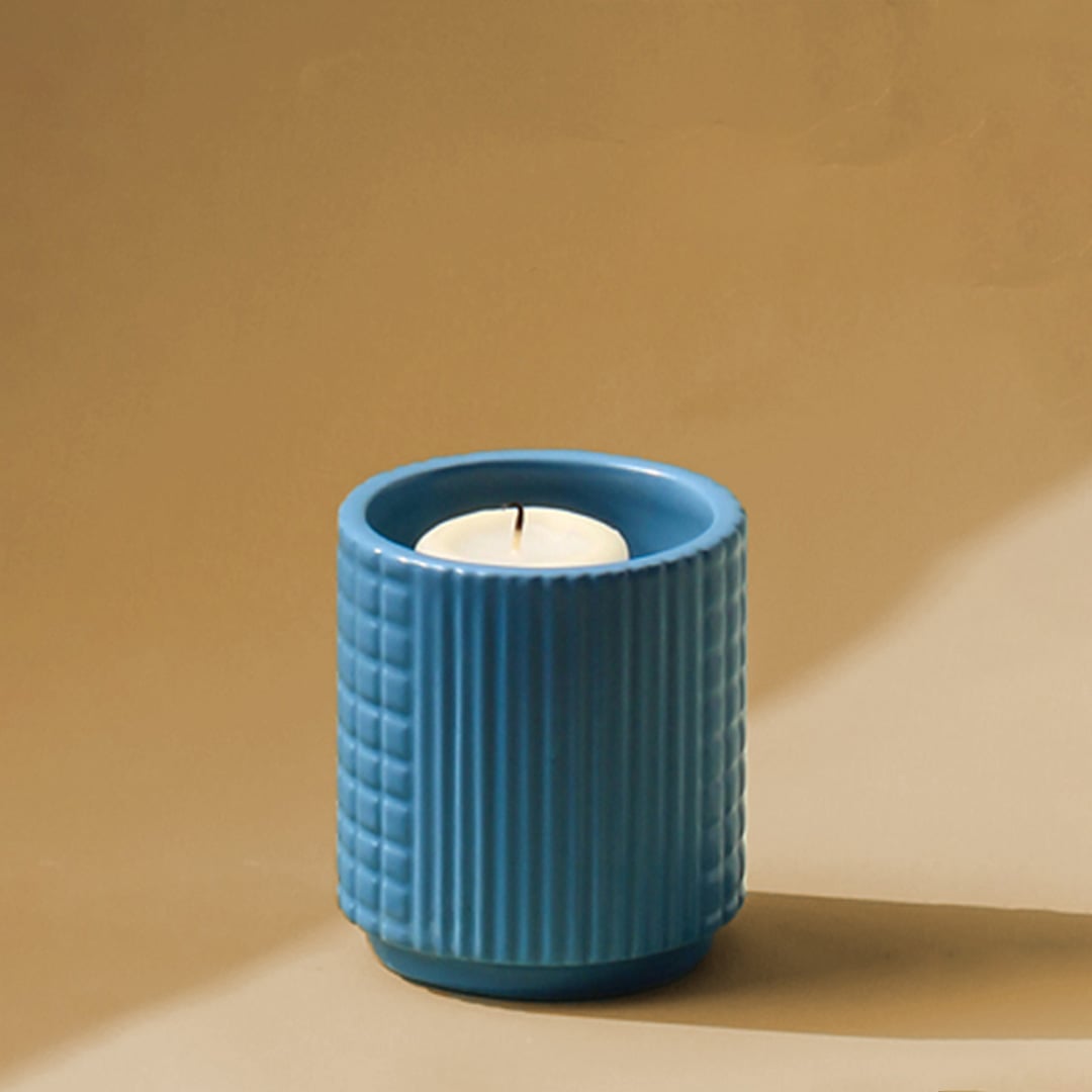 Closeup of ribbed blue ceramic candle holder with lit candle showing textured surface and modern tabletop decor styling.