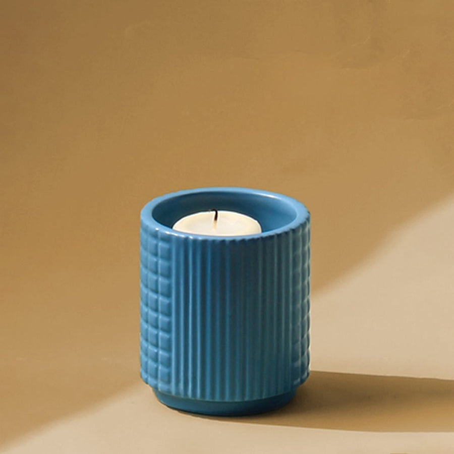 Closeup of ribbed blue ceramic candle holder with lit candle showing textured surface and modern tabletop decor styling.