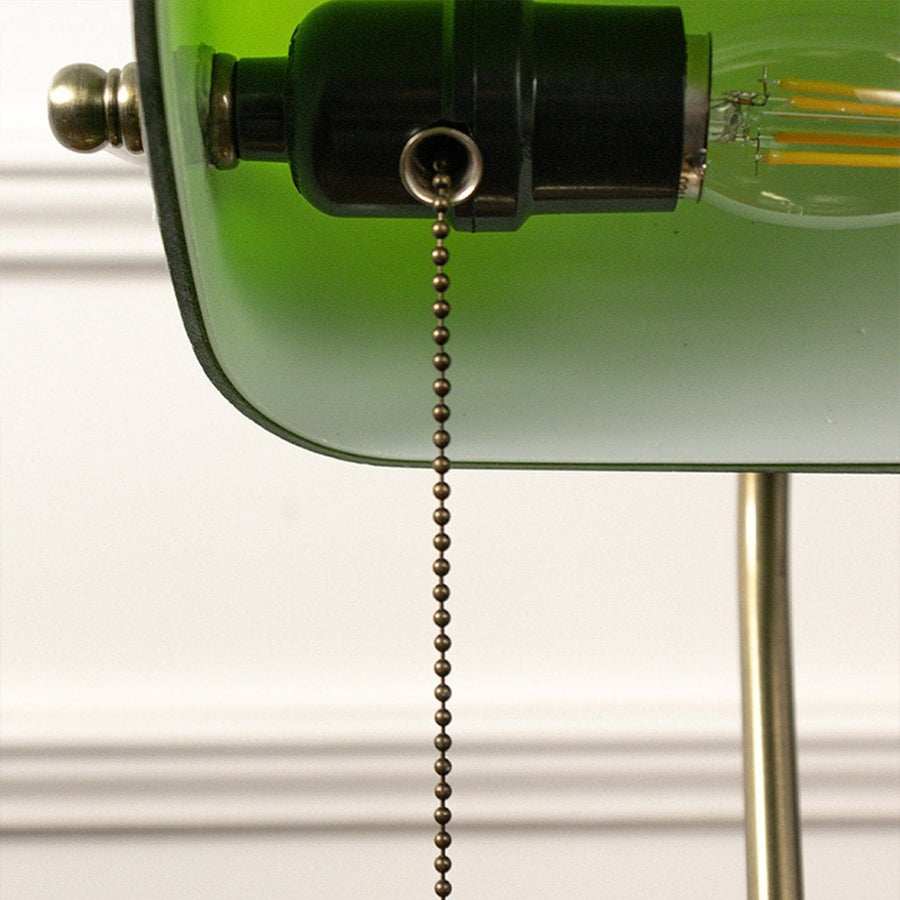 Macro shot of brass base and green glass top of banker table lamp revealing elegant texture and vintage finish.