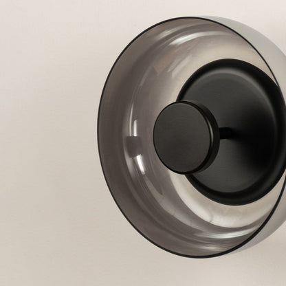 Detailed macro view of a contemporary round smoke glass wall lamp showcasing the matte black metal centerpiece mount.