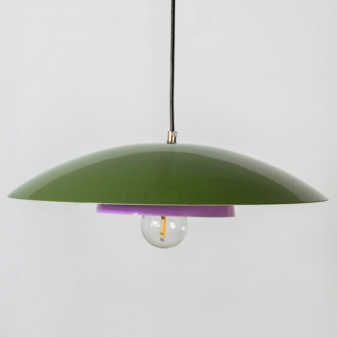 Closeup of green metal pendant light showing lavender inner plate and smooth dome for modern home interior decor.