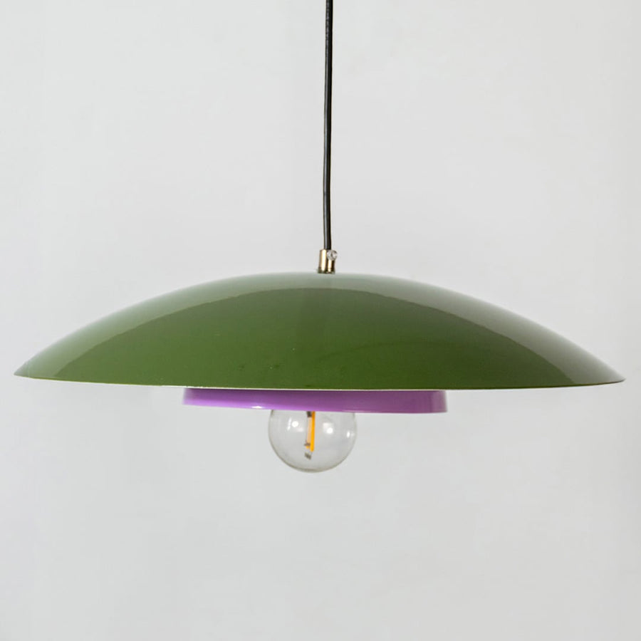 Closeup of green metal pendant light showing lavender inner plate and smooth dome for modern home interior decor.