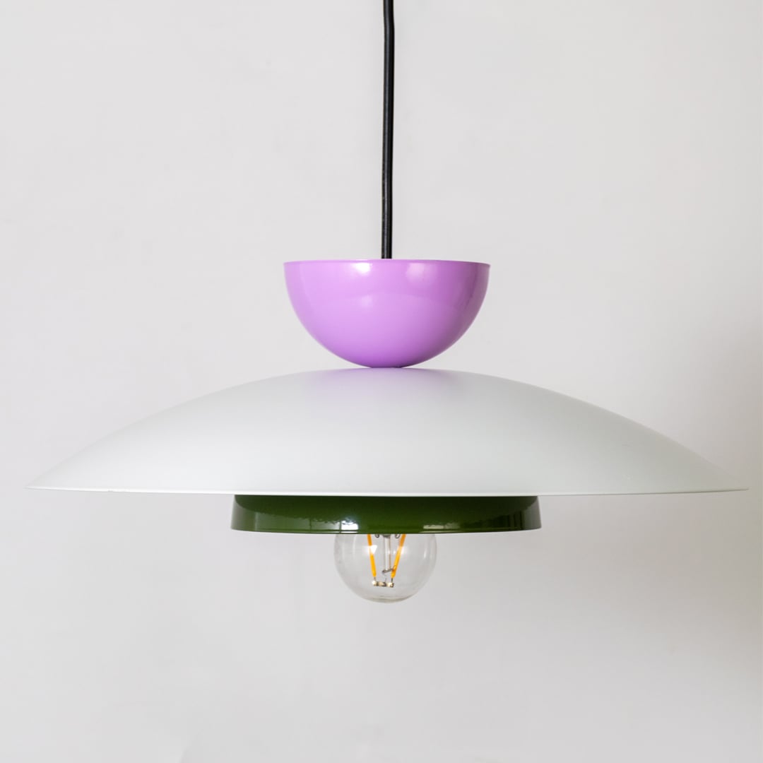 Closeup of multicolor metal pendant light showing white dome green ring and purple top for modern home interior decor.