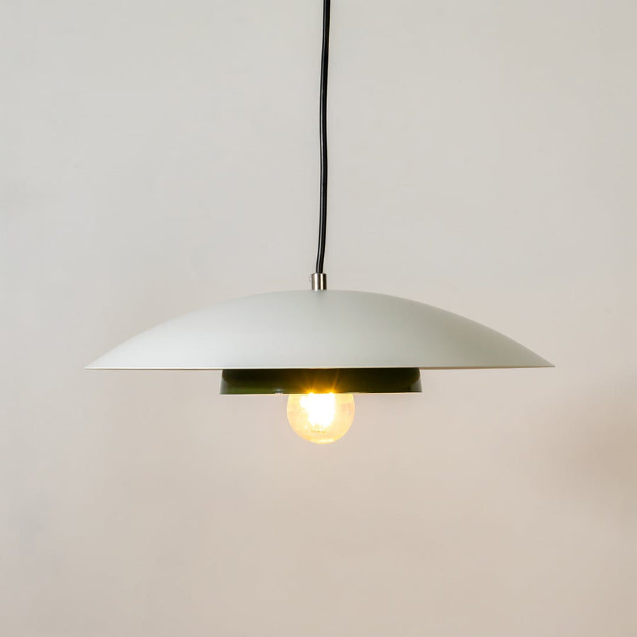 White metal pendant light glowing softly with green inner plate on white background for modern kitchen dining home decor.