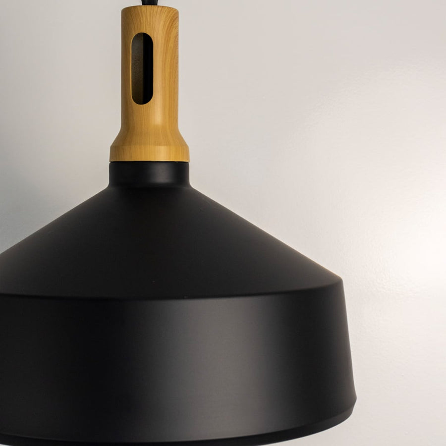 A closeup view of a black pendant light showing the wooden top and smooth matte shade with clean detailing that highlights its minimal modern design.