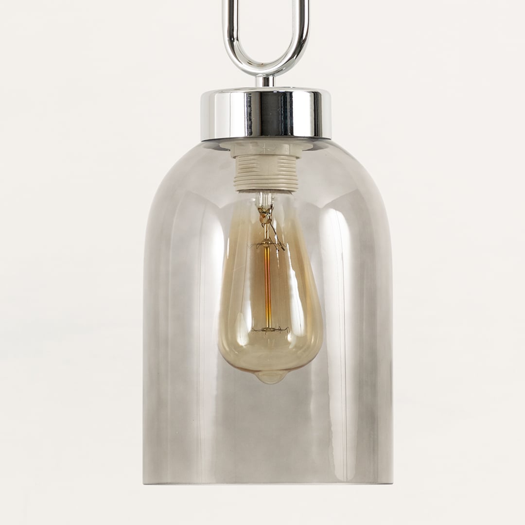 Closeup of smoked glass pendant emphasizing clean contours glossy metal accents and the warm bulb glow for modern aesthetic appeal.